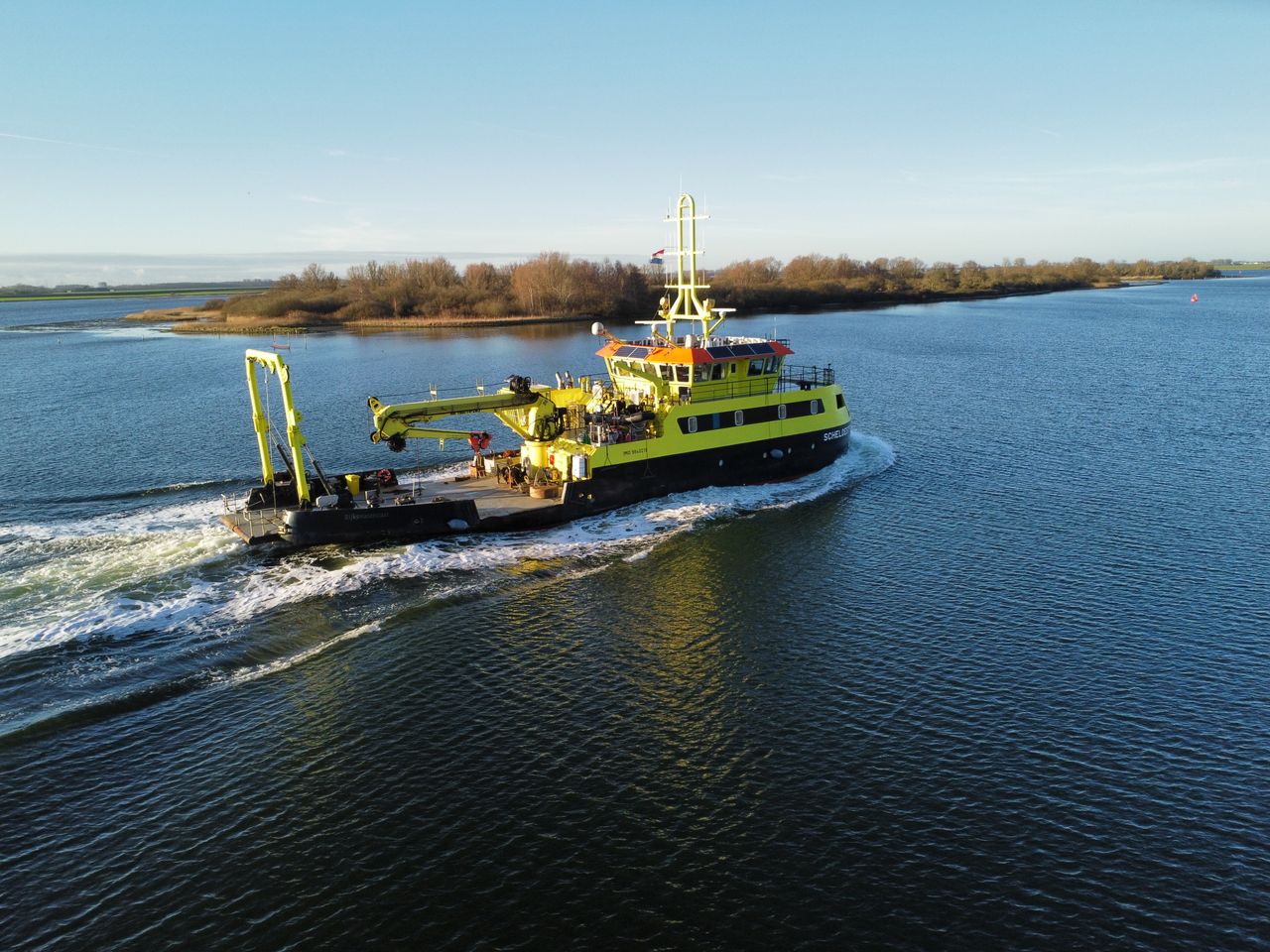 A vibrant yellow research vessel navigating through the clear waters near Kortgene, Netherlands.