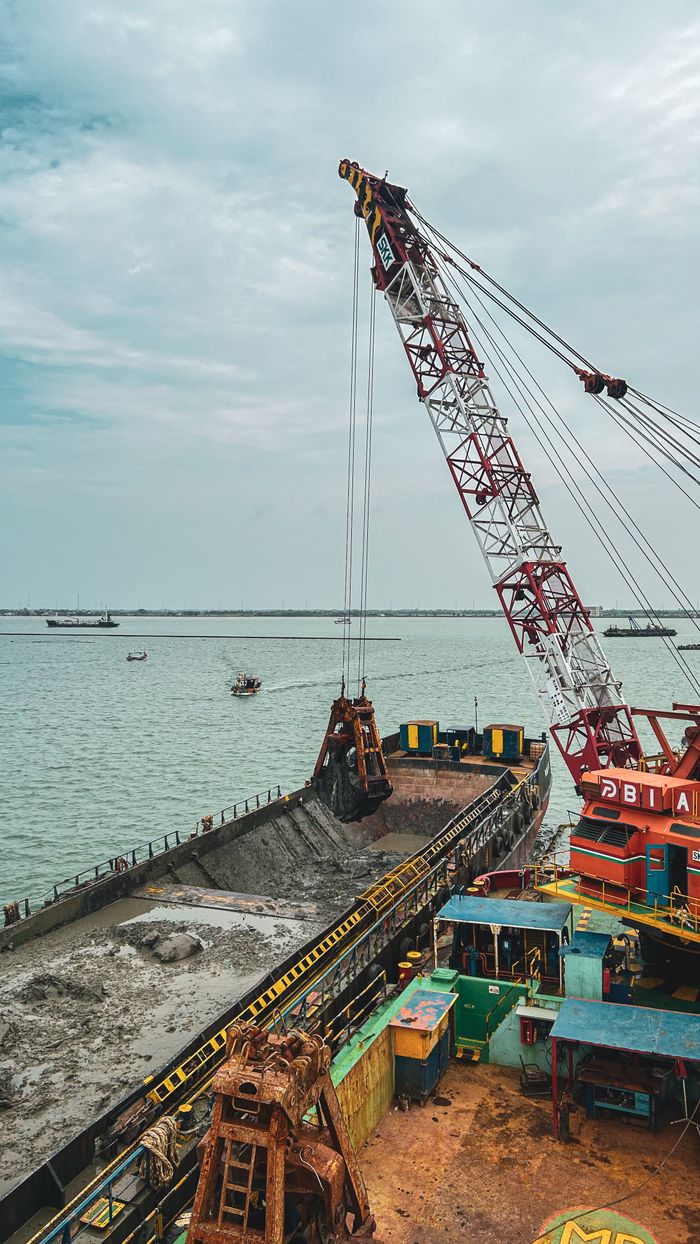 A large crane operating on a vessel during an industrial dredging operation in a harbor.