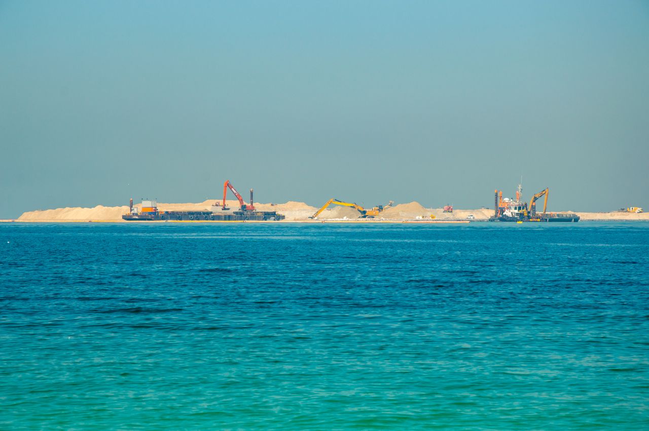 Distant view of an offshore construction site with machinery and clear blue sea.