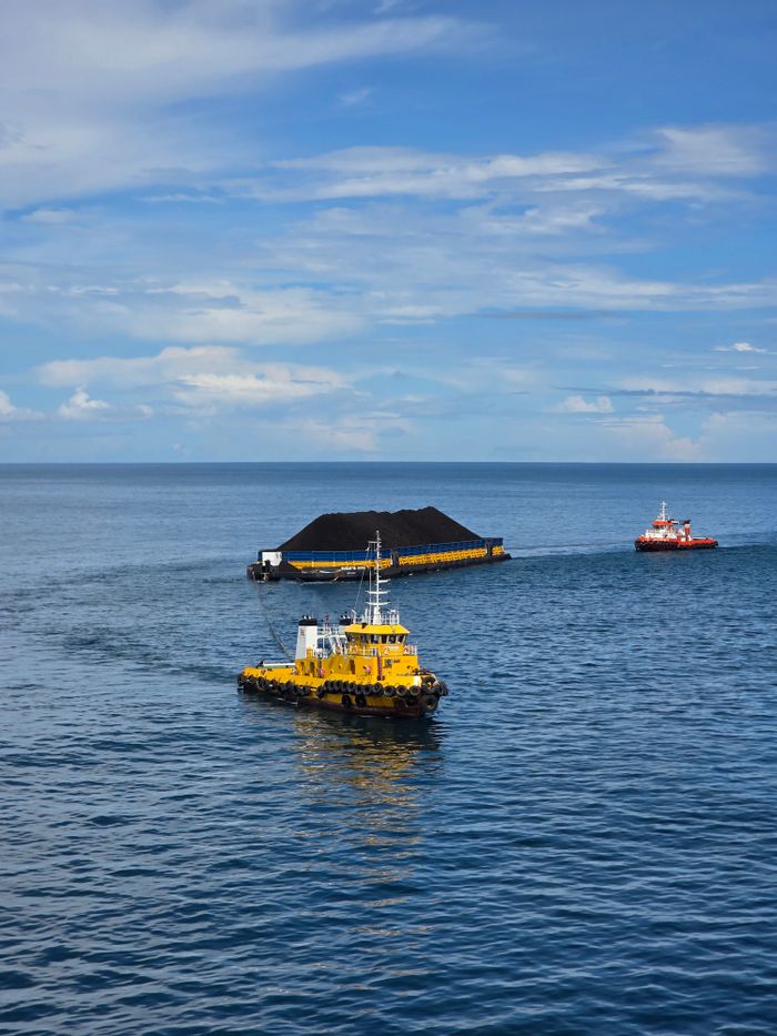 Yellow tugboat guiding a coal barge on the blue waters of Indonesia under clear skies.